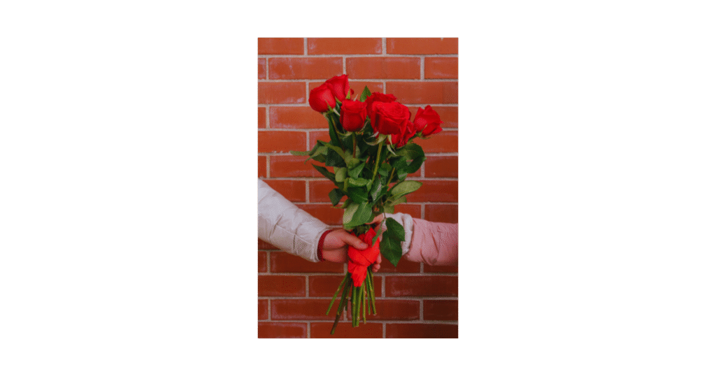 two hands holding a bouquet of red roses against a brick wall