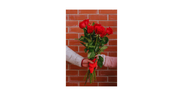 two hands holding a bouquet of red roses against a brick wall