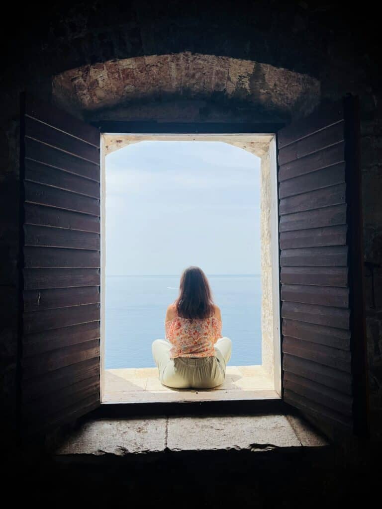 A woman in her late forties sitting by an open window, looking calm and directly ahead